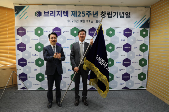 지난달 31일 브리지텍 창립기념일 행사에서 이상호(왼쪽)전  브리지텍 대표가 신경식 신임 브리지텍 사장에 회사기를 넘겨주며 기념촬영을 하고 있다.    브리지텍 제공